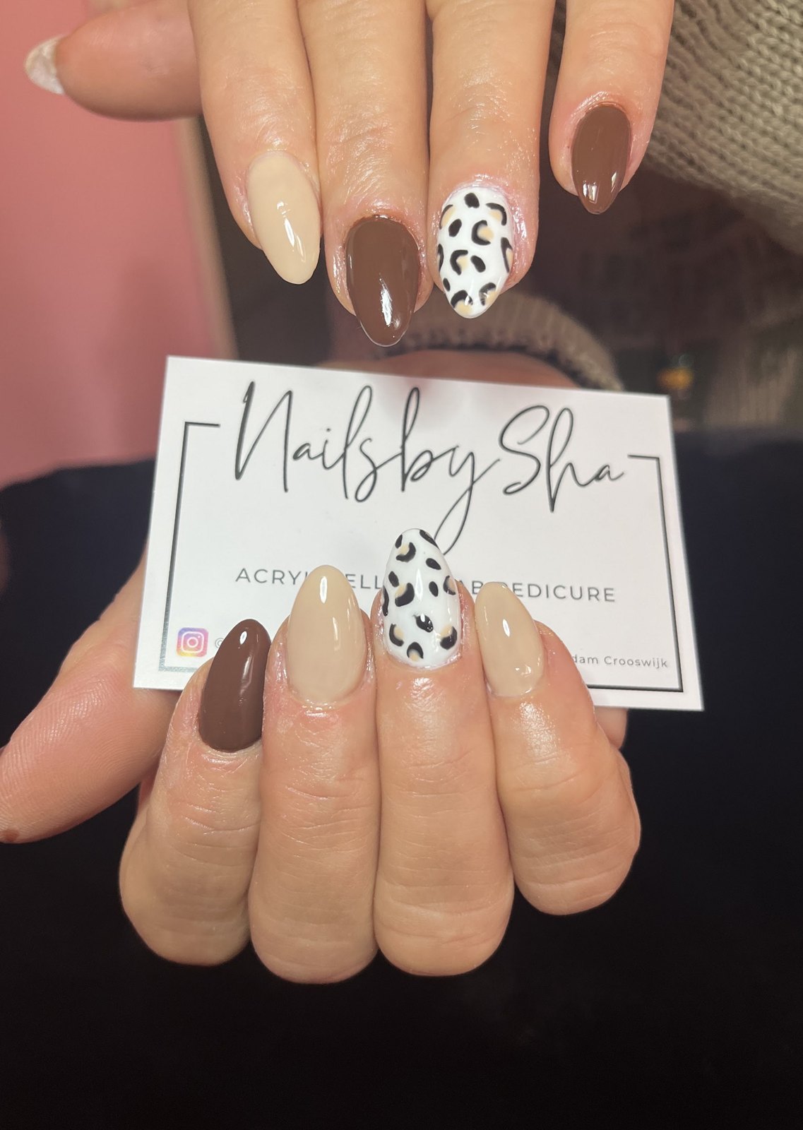 Amandelvormige nagels in bruin, nude en een luipaardprint, met het visitekaartje van Nailsbysha in de hand