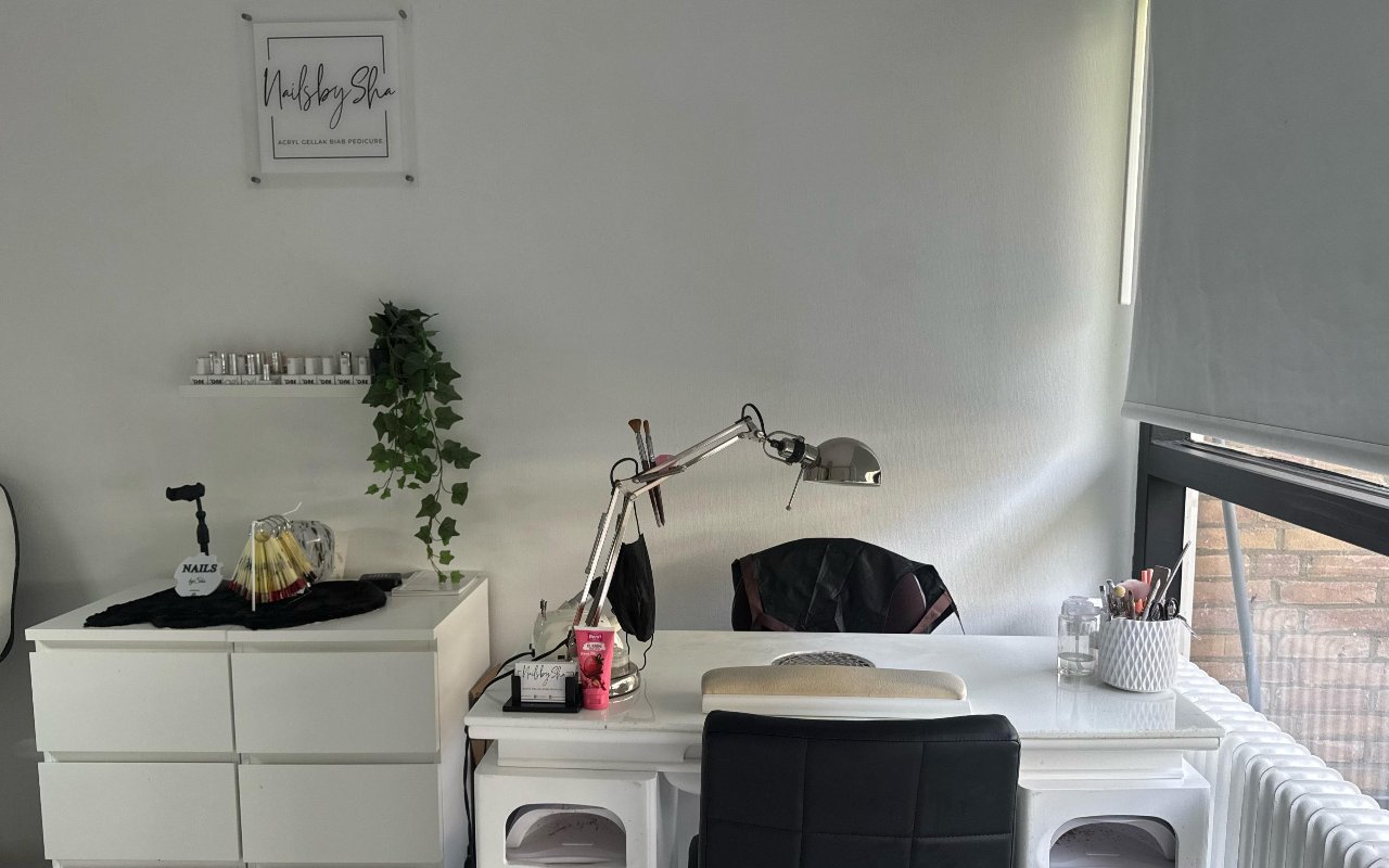 De witte werkplek van Nailsbysha met het logo aan de muur