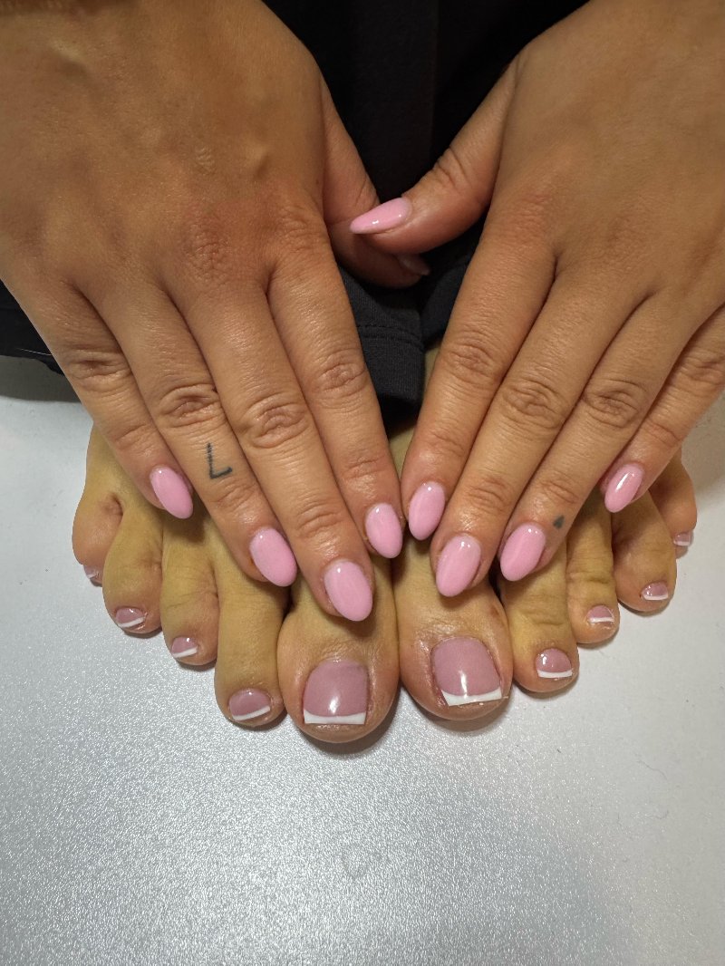 Handen met roze nagels boven voeten met een witte French op de tenen